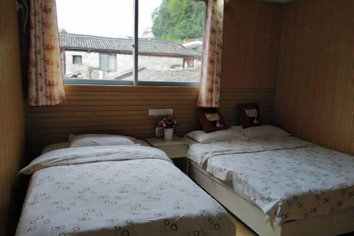 Una habitació amb dos llits, parets de fusta, una finestra amb cortines i una taula petita amb un vas de flors.