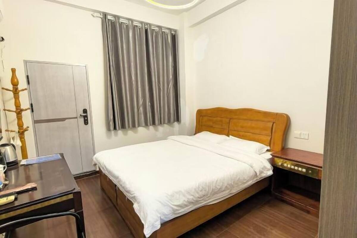Une chambre à coucher avec un lit en bois, un bureau, une chaise, une armoire et un rideau.