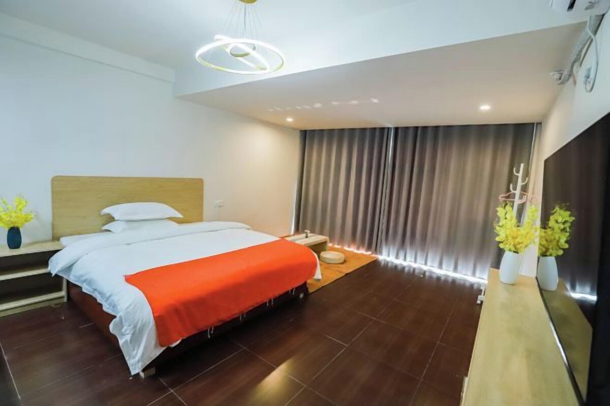 Ein modernes Hotelzimmer mit einem Bett, einem Nachttisch, einem kleinen Hocker und einem großen Fenster mit Vorhängen.