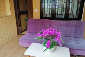 Um sofá roxo com uma mesa branca na frente, um vaso roxo com flores cor-de-rosa e um chão de madeira.