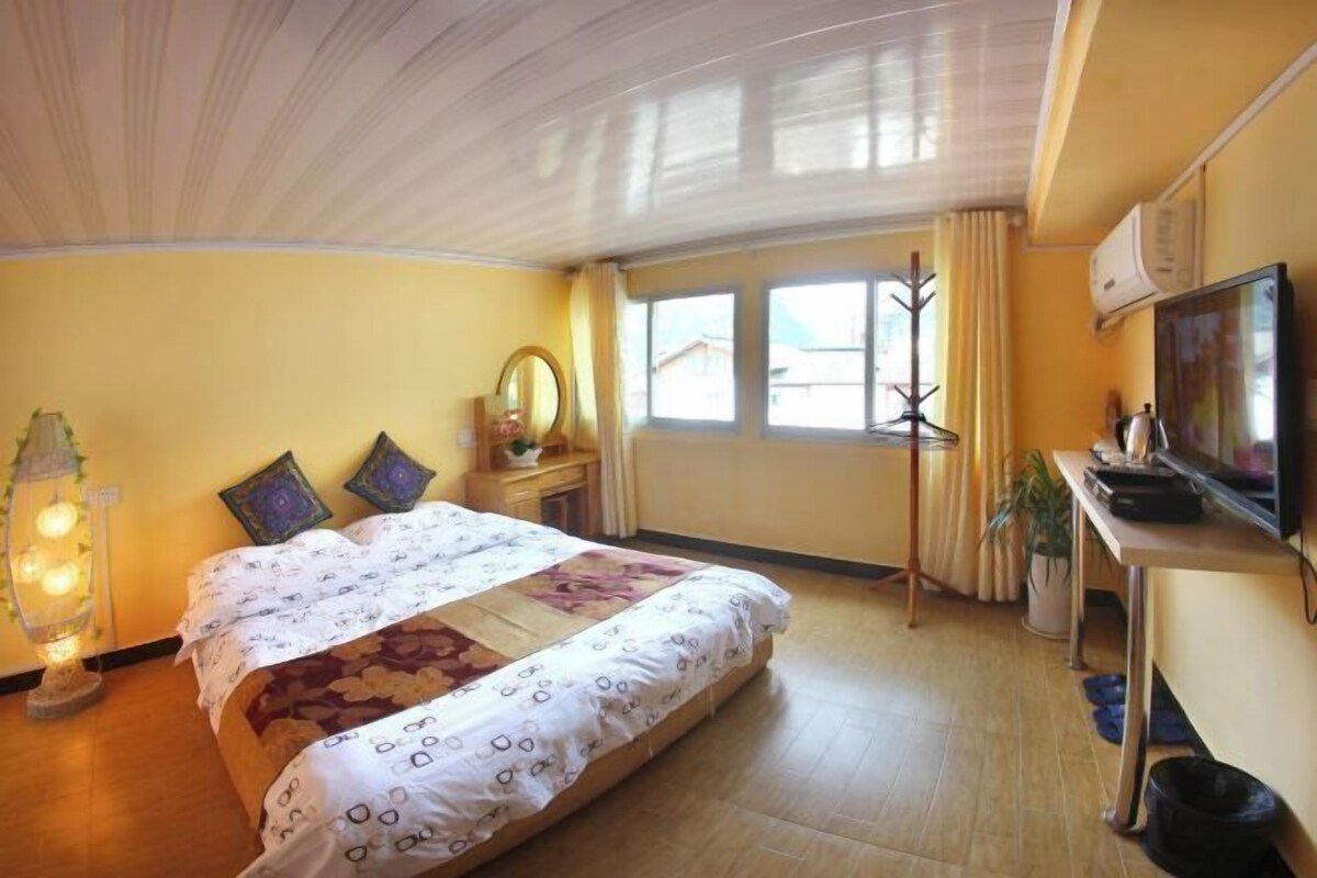 Habitació d'hotel amb un llit, una taula de treball, una televisió i una finestra amb cortines.