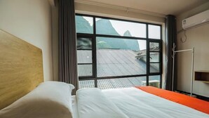 Une chambre d’hôtel avec un lit, une fenêtre donnant sur les montagnes et un appareil de climatisation.