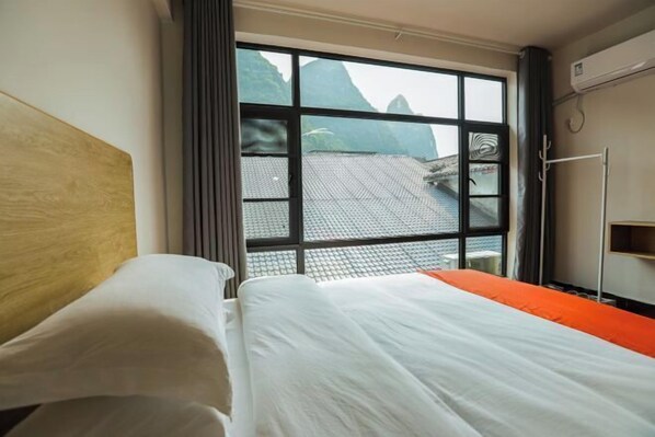 Habitació d'hotel amb un llit, una finestra que dona a les muntanyes i un aparell d'aire condicionat.