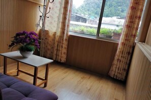 A room with a wooden floor, a purple sofa, a small table with a plant, and a window with curtains.