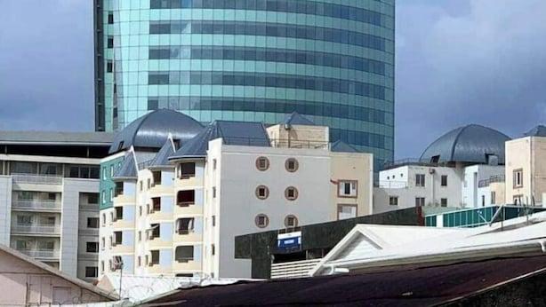 En moderne skyskraber med en buet glasfacade, omgivet af andre bygninger med flade tage og en klar himmel.