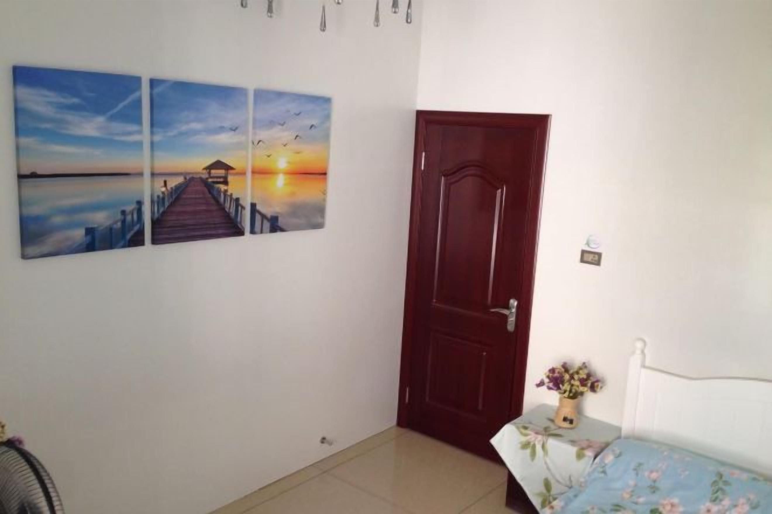 Una stanza con un letto, una porta in legno e un muro decorato con tre quadri.