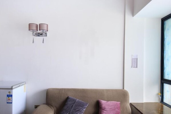A modern room with a beige sofa, two cushions, a small table, and a wall-mounted light fixture.