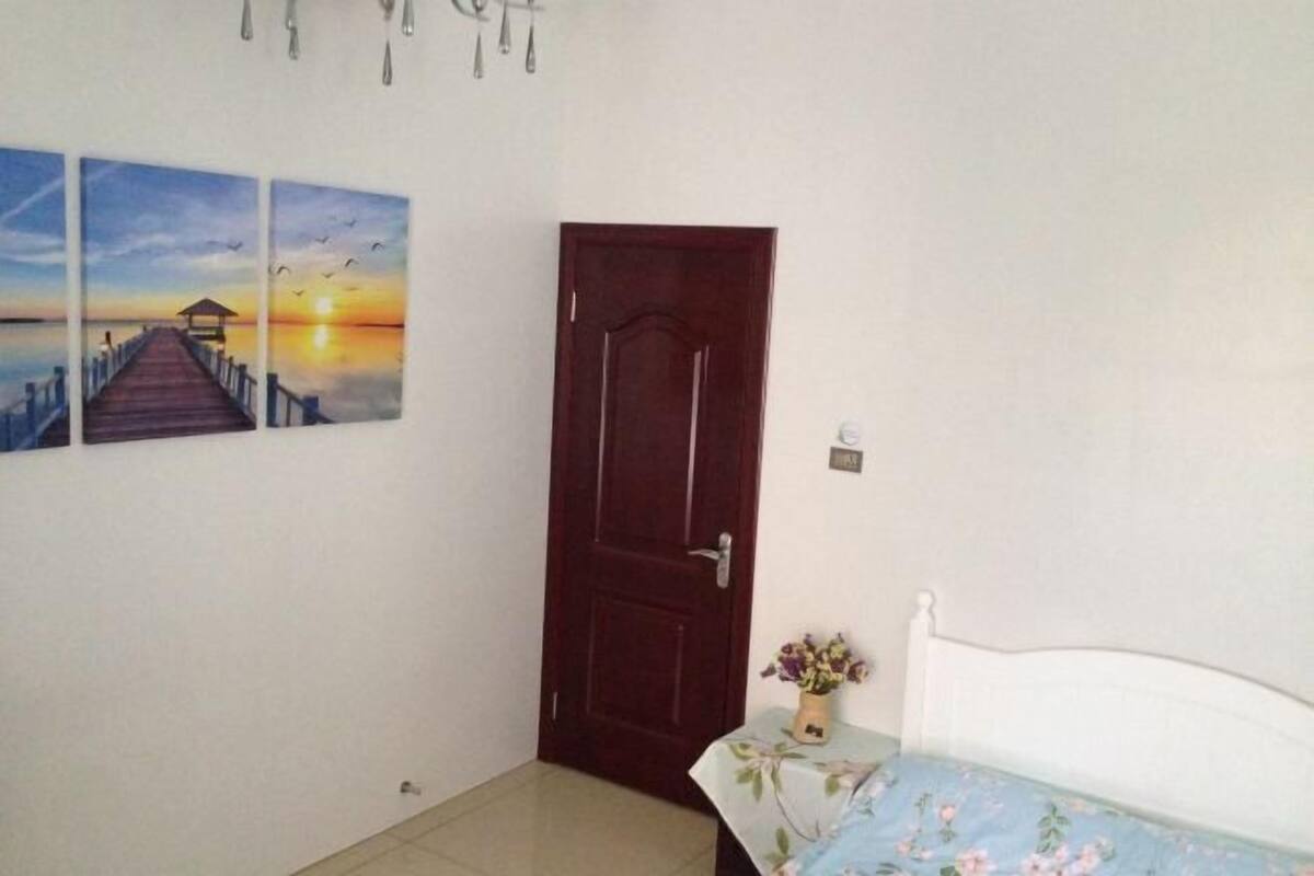 Ein Schlafzimmer mit einem Bett, einer Holztür und zwei an der Wand befestigten Bildern eines Sonnenuntergangs über einem Steg.