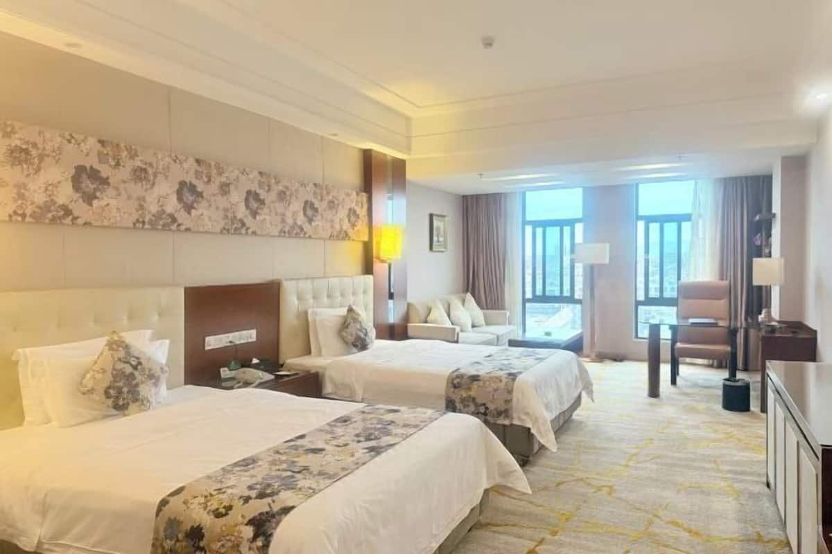 Une chambre d’hôtel avec deux lits, un canapé, un bureau et une grande fenêtre.