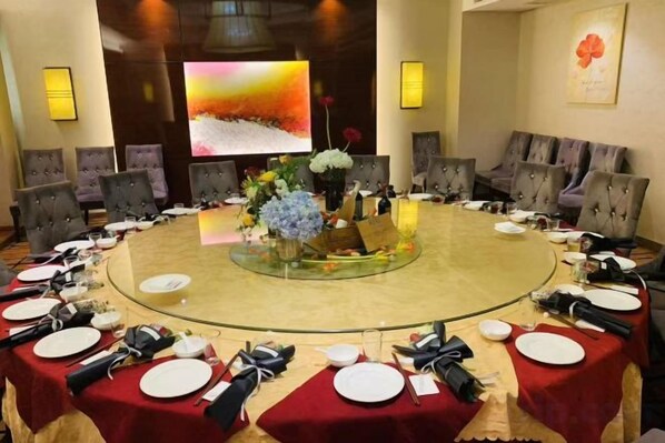 Un salón de conferencias con una mesa redonda, sillas y una pantalla grande.