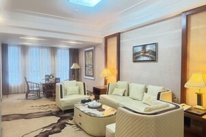 Habitación de hotel con sofá, mesa de comedor con sillas, mesa de centro y un cuadro en la pared.