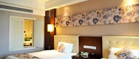 A hotel room with two beds, a large floral-patterned headboard, a nightstand, and a mirror.