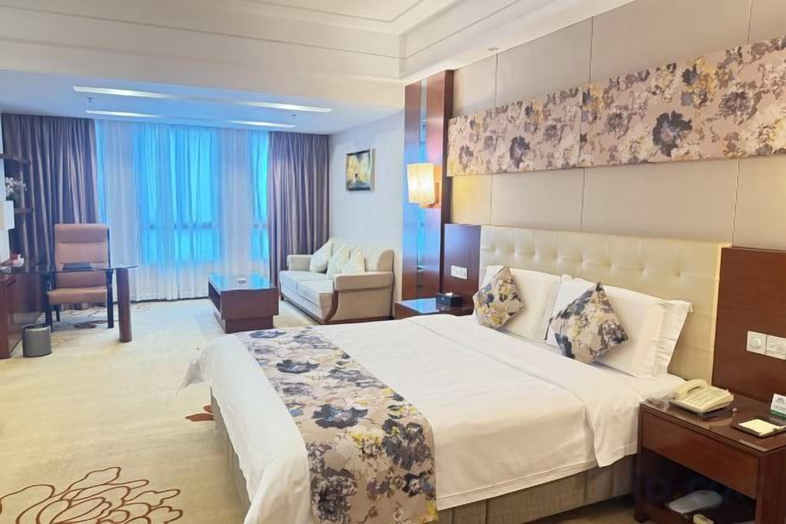 A hotel room with a large bed, a desk, a chair, a sofa, and a view of the outdoors.