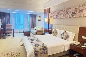 Habitación de hotel con una cama grande, escritorio, sillón, sofá y vistas al exterior.