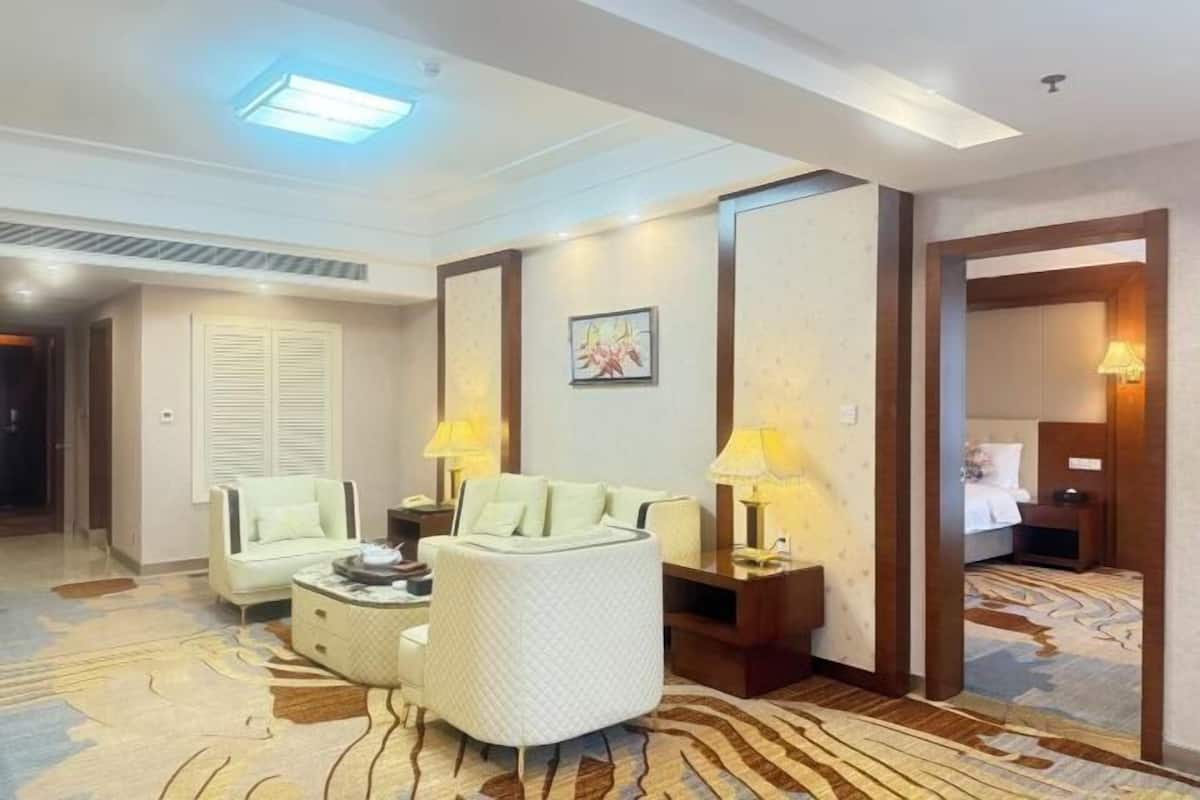 Une chambre d’hôtel équipée d’un canapé, d’un fauteuil, de tables de chevet et d’un tapis à motifs.