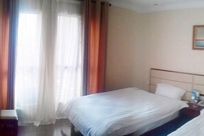 Quarto de hotel com uma cama de solteiro, mesa de cabeceira e janela com cortinas.
