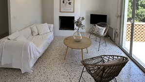 A modern living room with a white sofa, a round coffee table, and a wicker chair. There's a framed botanical print on the wall and a fireplace below it. - Pleasant house in a quiet area, swimming pool, air conditioning, WIFI, max 12 pers. (Uchaux)
