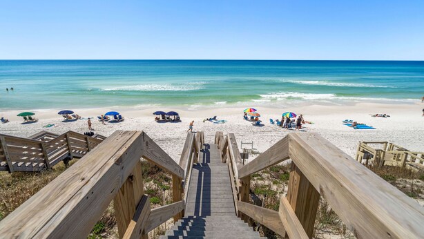 A wooden staircase leading to a beach with umbrellas and lounge chairs.