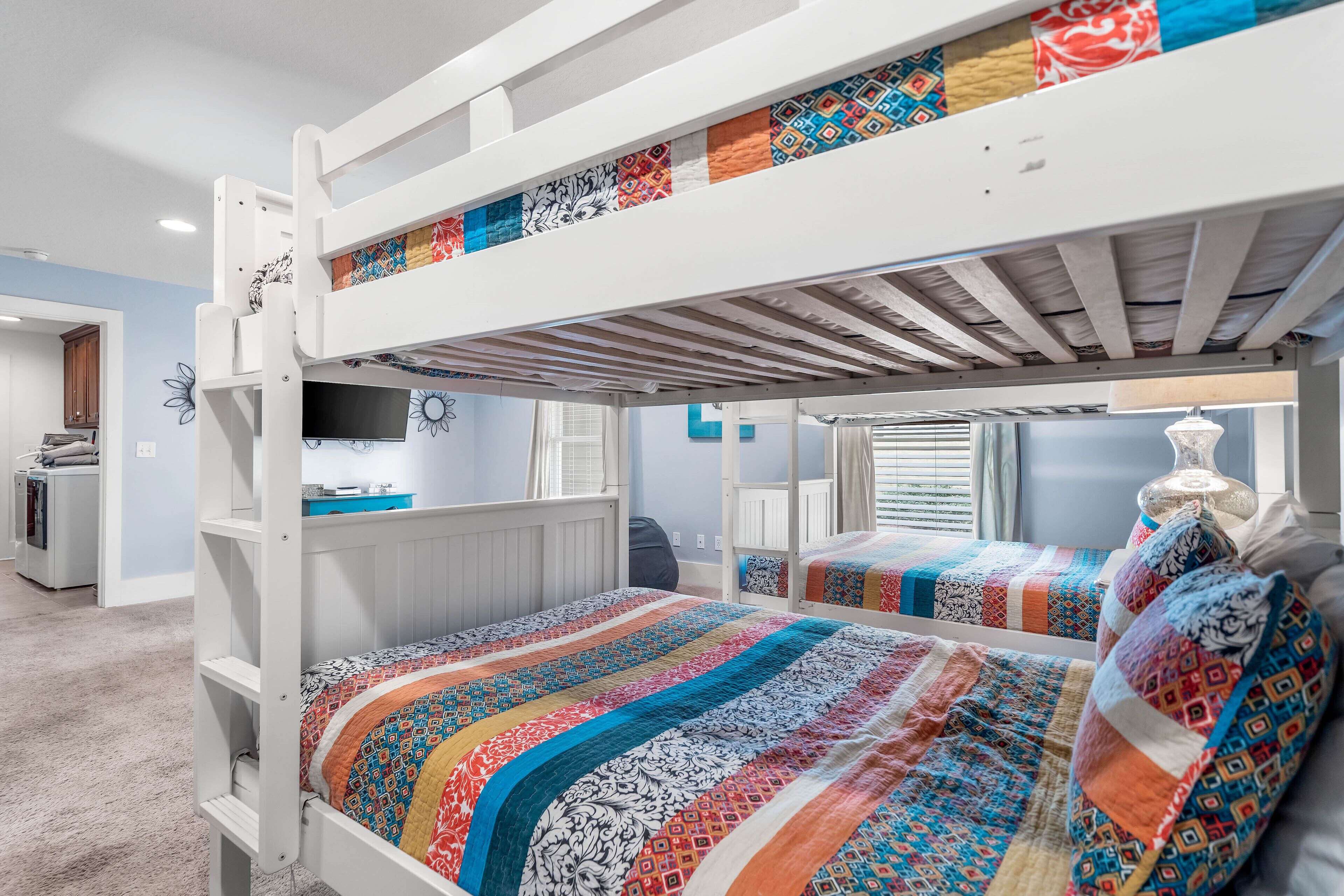 Habitación con literas, una colcha colorida, un escritorio y un espejo.