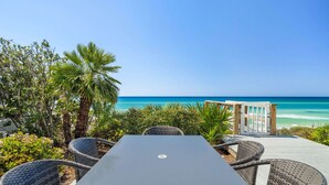 A seaside patio with a table and wicker chairs, overlooking the ocean.