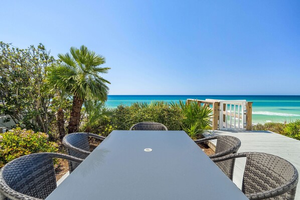 A seaside patio with a table and wicker chairs, overlooking the ocean.