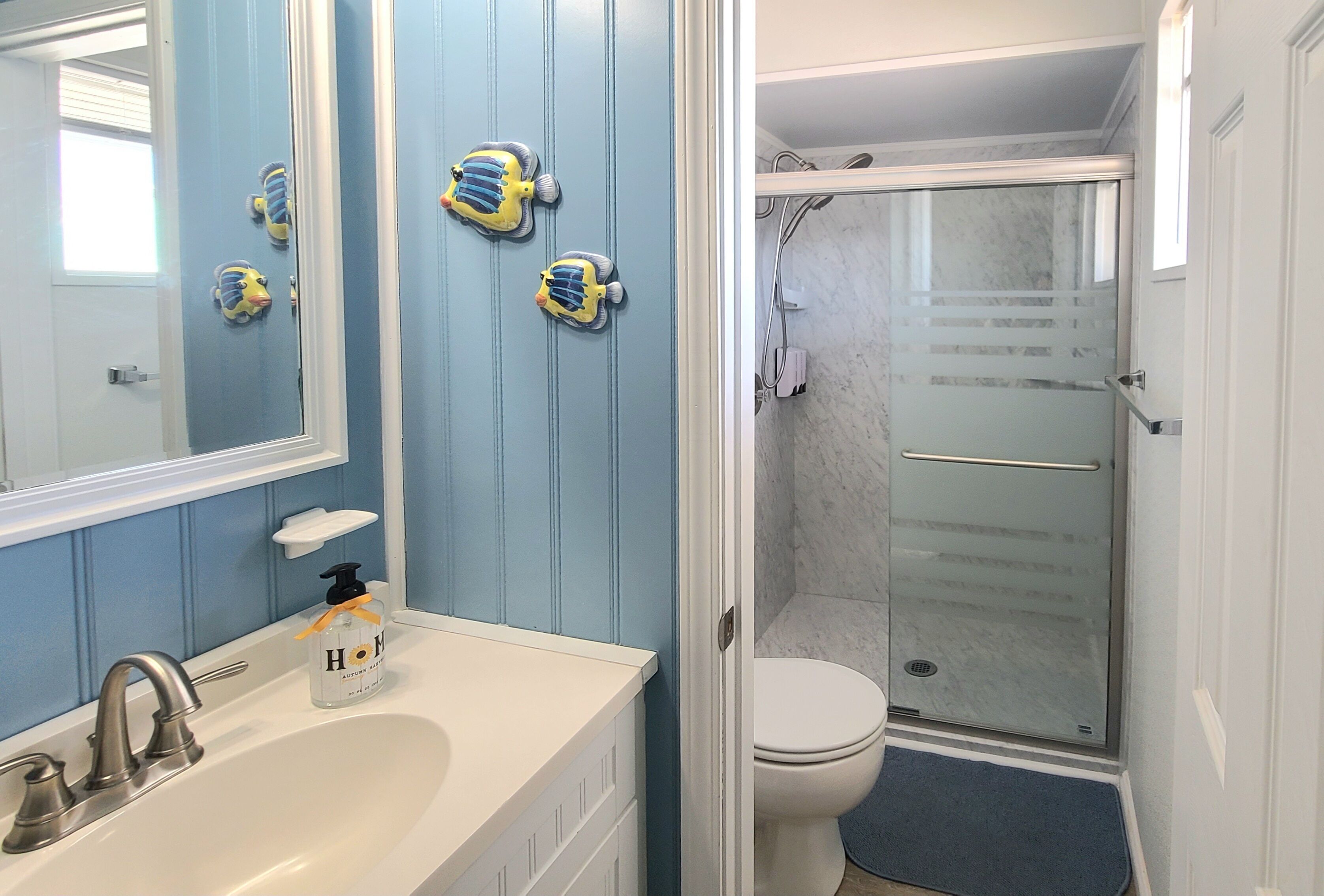 Une salle de bain avec un lavabo blanc, des murs bleus et une douche en verre.