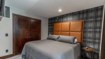 A bedroom with a large bed, a wooden wardrobe, a headboard with a padded section, and a small bedside table with a lamp.
