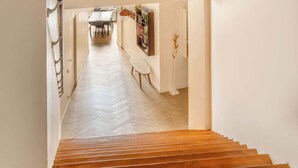 A staircase leading to a room with a herringbone floor, a hanging light fixture, and a wall-mounted artwork.
