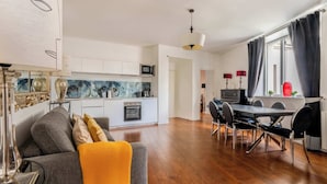 Un salon moderne comprenant un canapé, une table à manger avec des chaises, un coin cuisine et une grande fenêtre avec des rideaux.