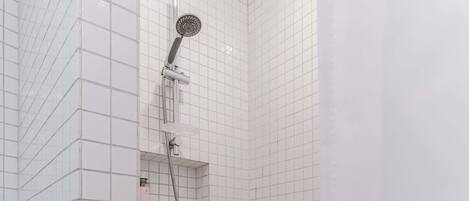 A shower with a handheld showerhead and a wall-mounted faucet, tiled walls, and a white bathtub.
