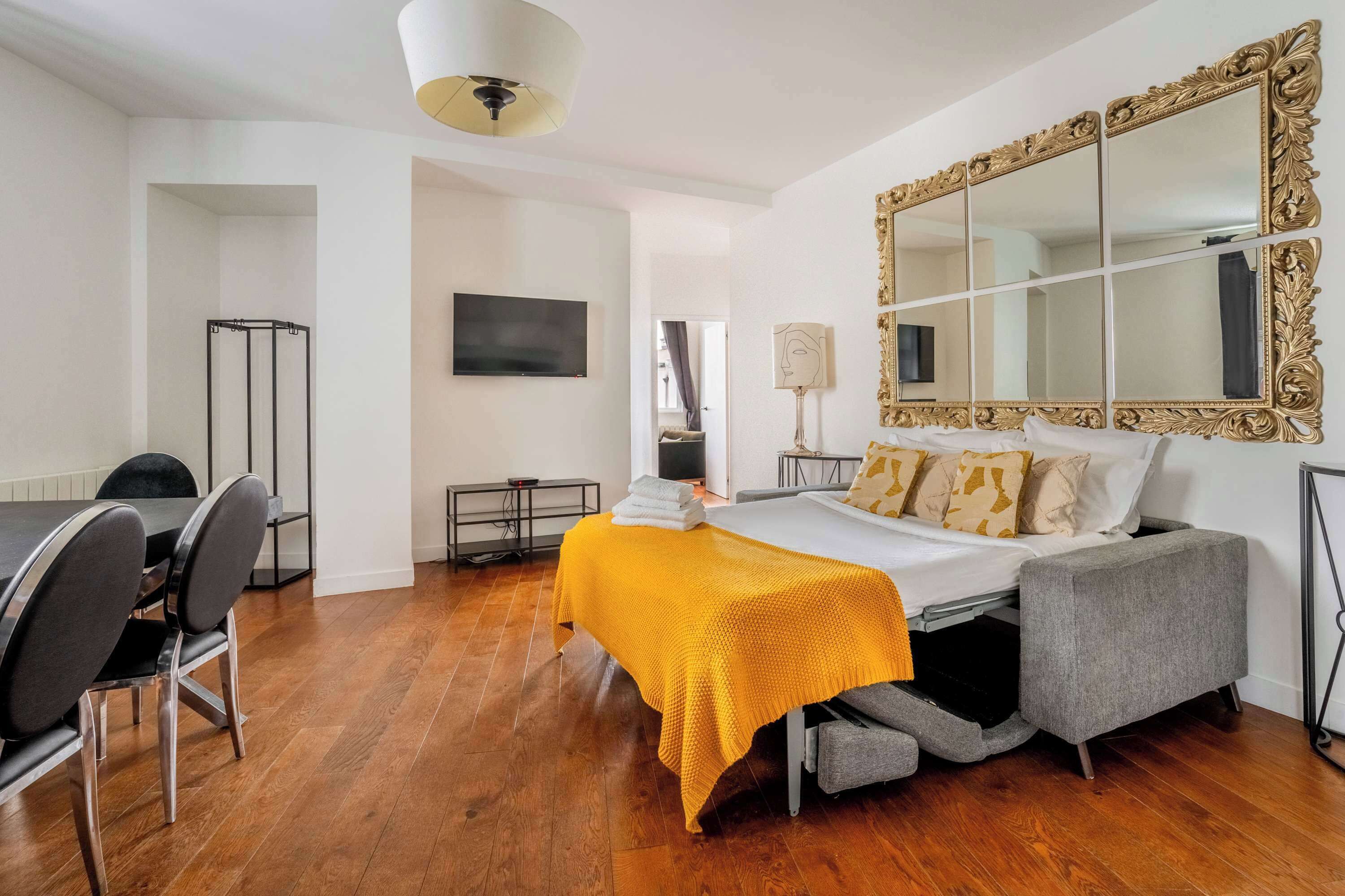 Une chambre à coucher comprenant un lit, un canapé, une télévision, un miroir et un coin repas avec des chaises et une table.