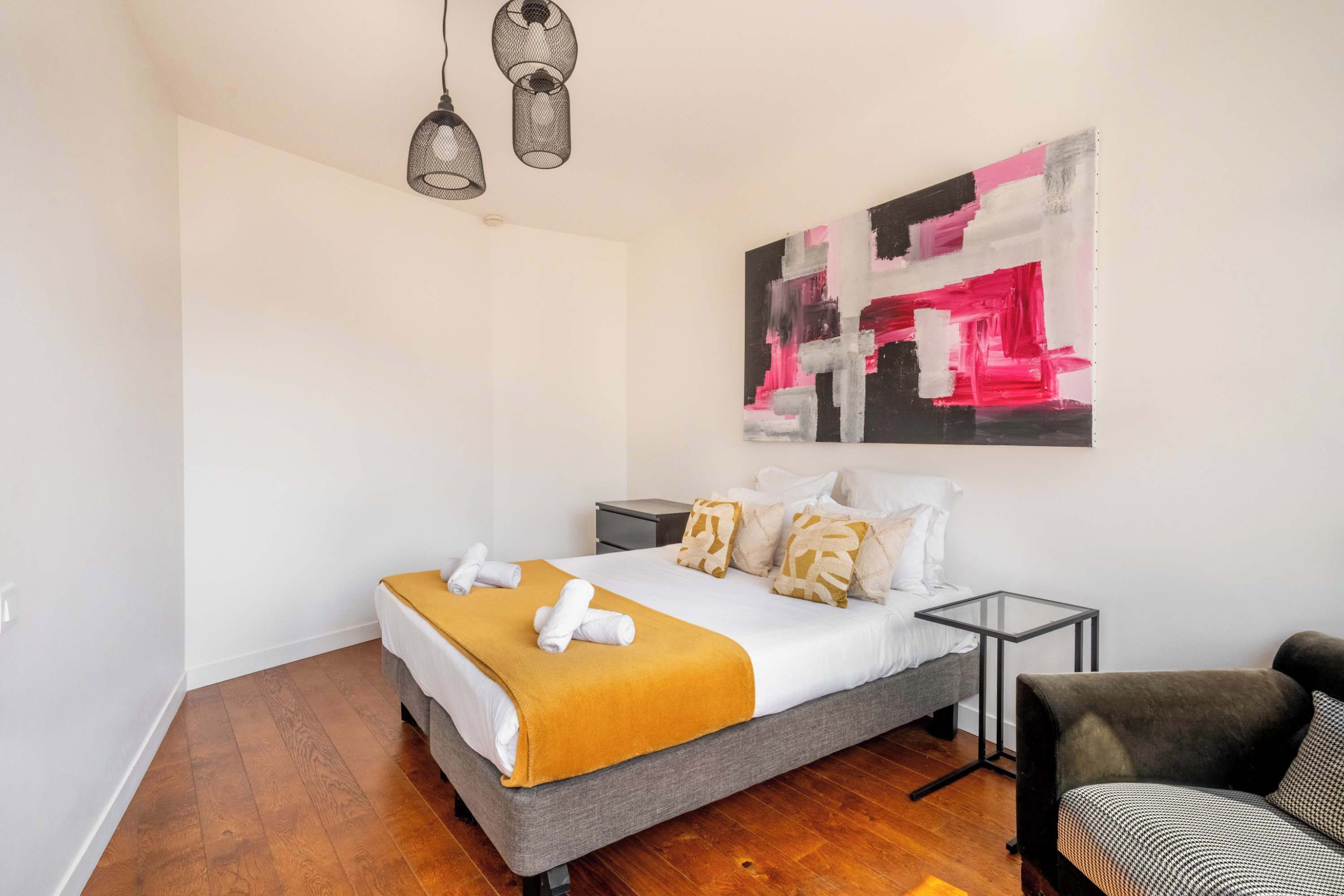 A modern bedroom with a bed, bedside tables, a chair, and a large abstract painting on the wall.