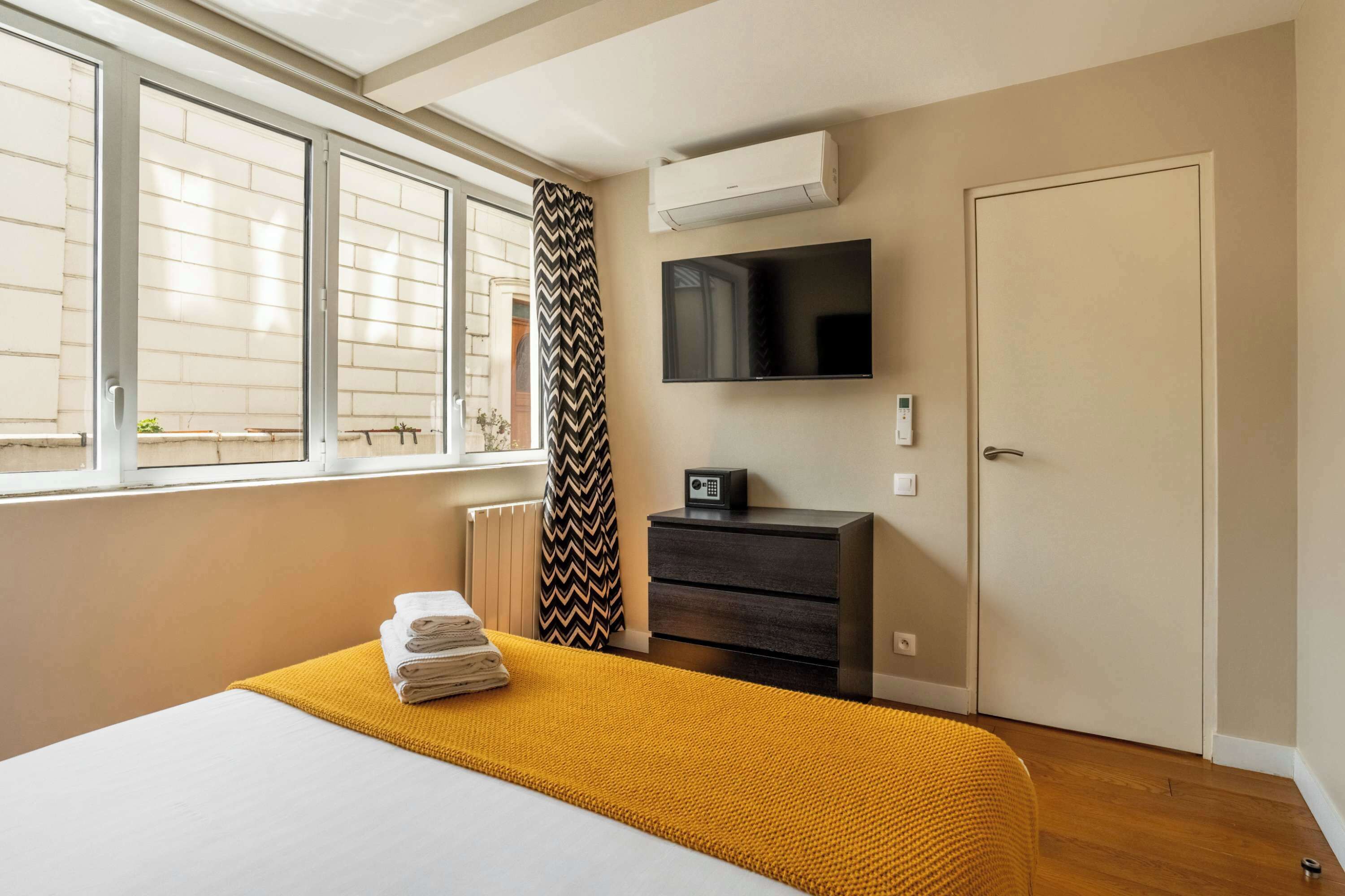 Ein Hotelzimmer mit Bett, Fernseher, Kommode und Fenster mit Jalousien.