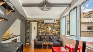 Un espace de vie compact comprenant une cuisine, un coin repas et un canapé agrémenté d’un papier peint à motifs.