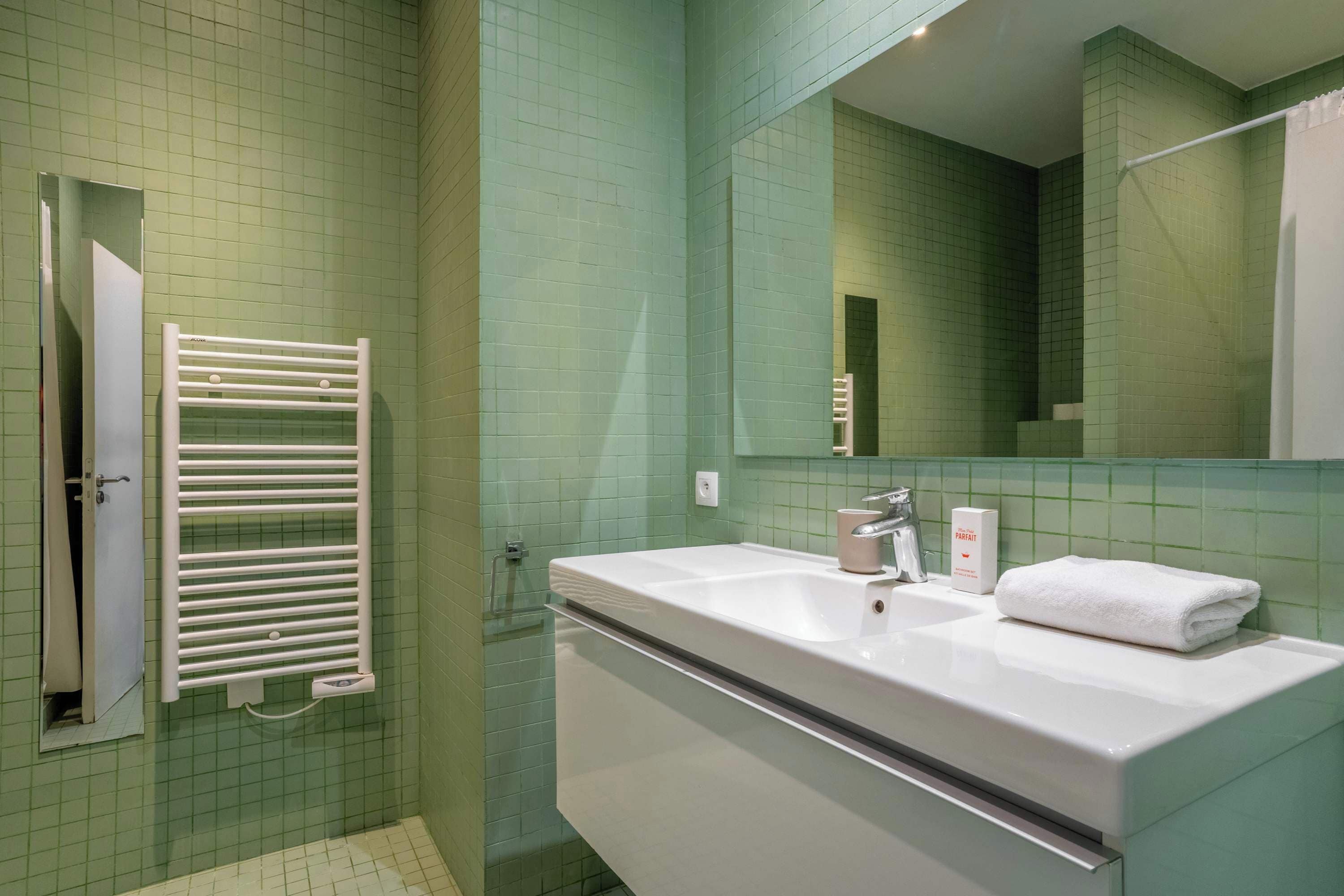 Un bagno con un lavandino bianco, uno specchio, un asciugamano e una zona doccia.
