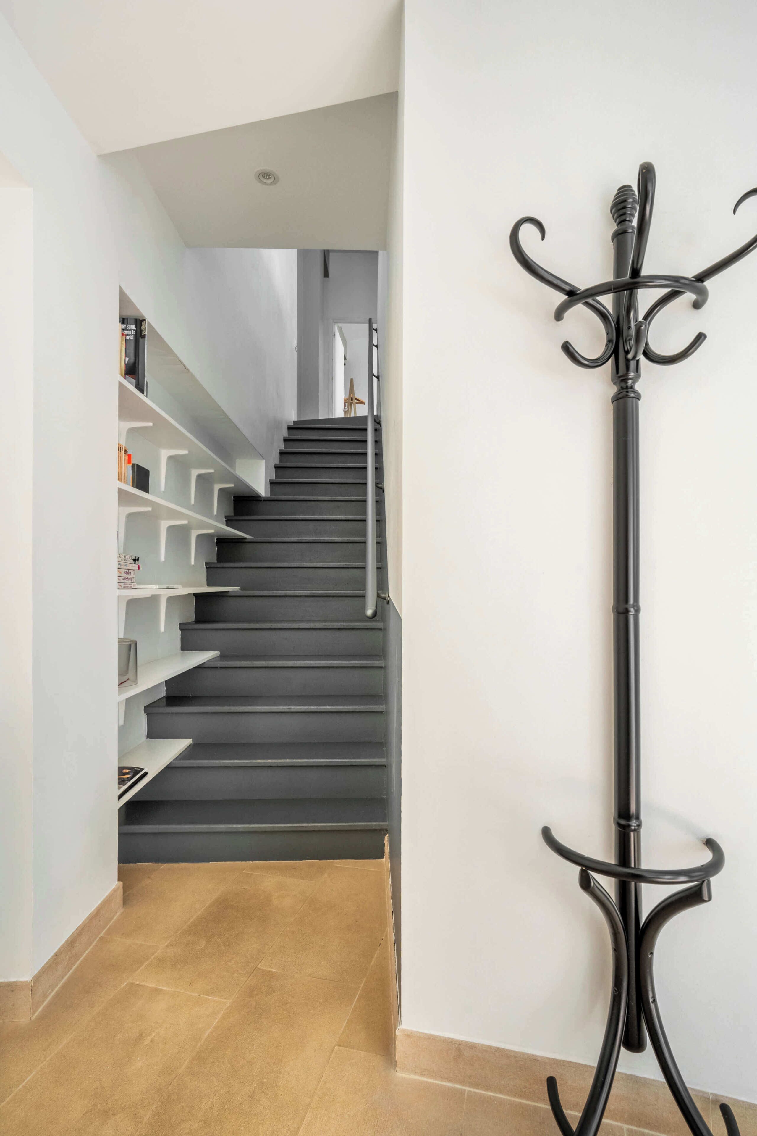 A staircase with a metal railing, a black coat stand, and white shelves on the left side.
