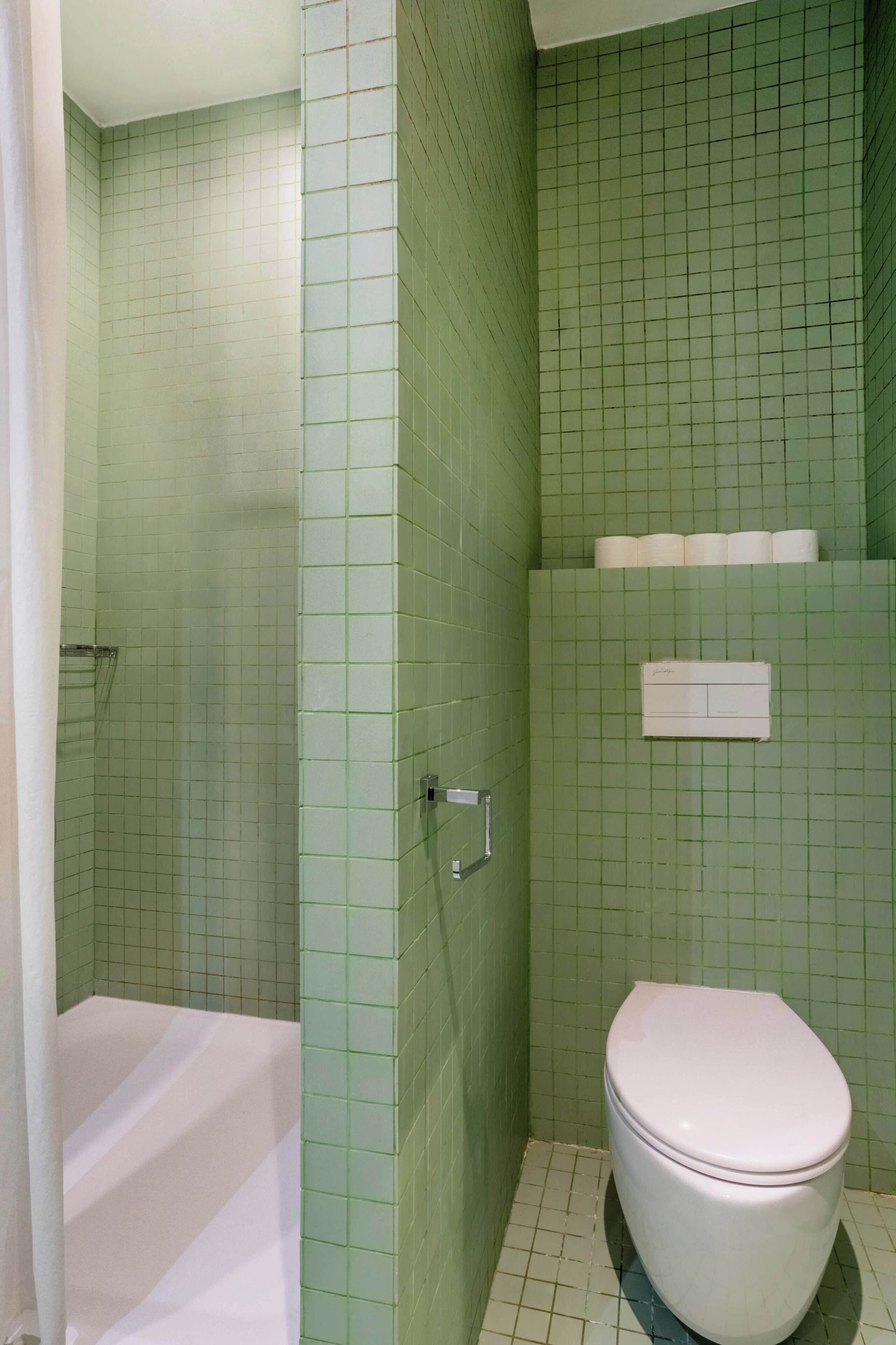 Een badkamer met groene betegelde wanden, een wit toilet en een bad.