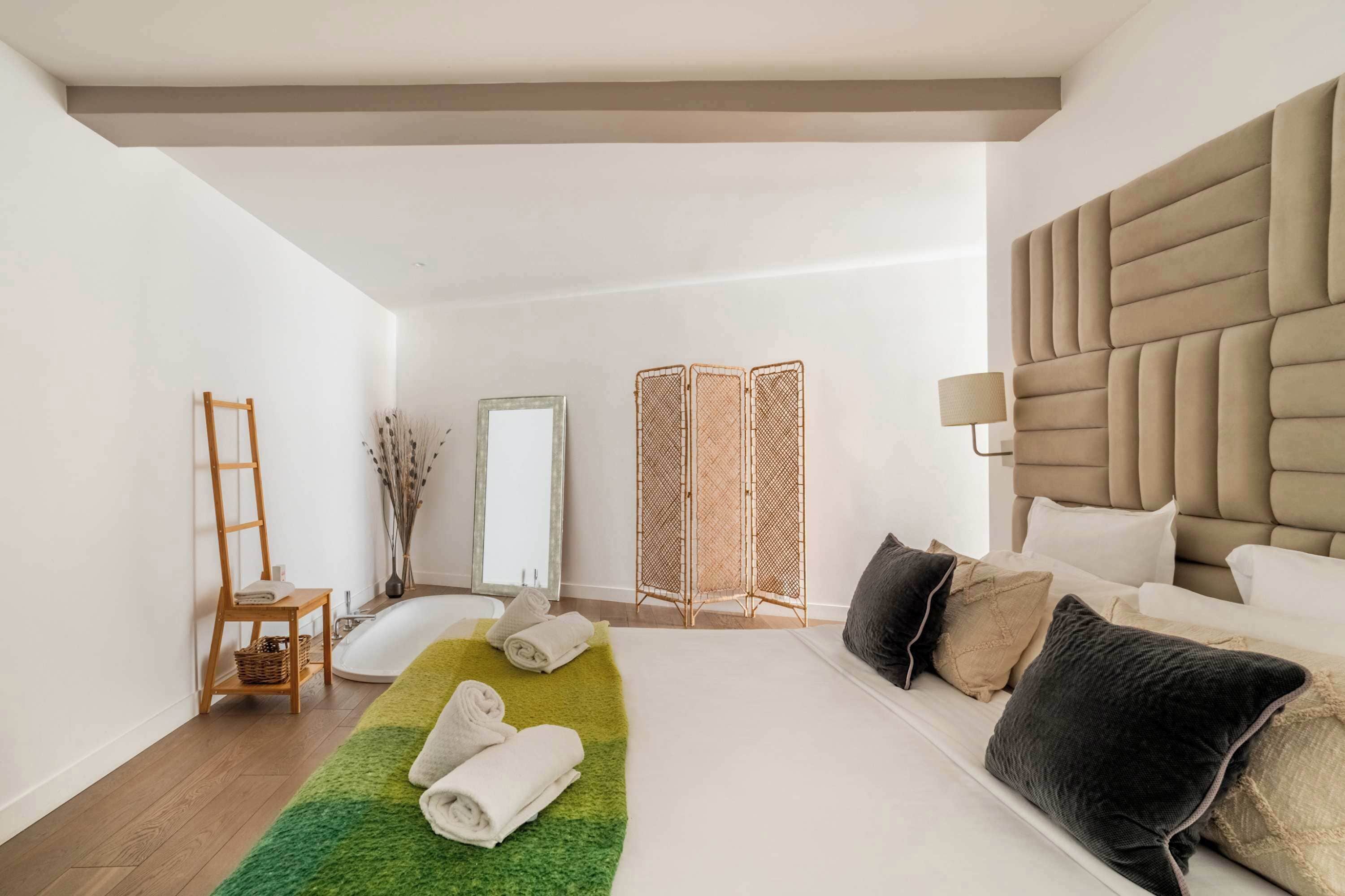 Ett modernt hotellrum med en stor säng, en trästege, en grön matta och en spegel.
