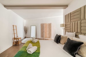 A modern hotel room with a large bed, a wooden ladder, a green rug, and a mirror.
