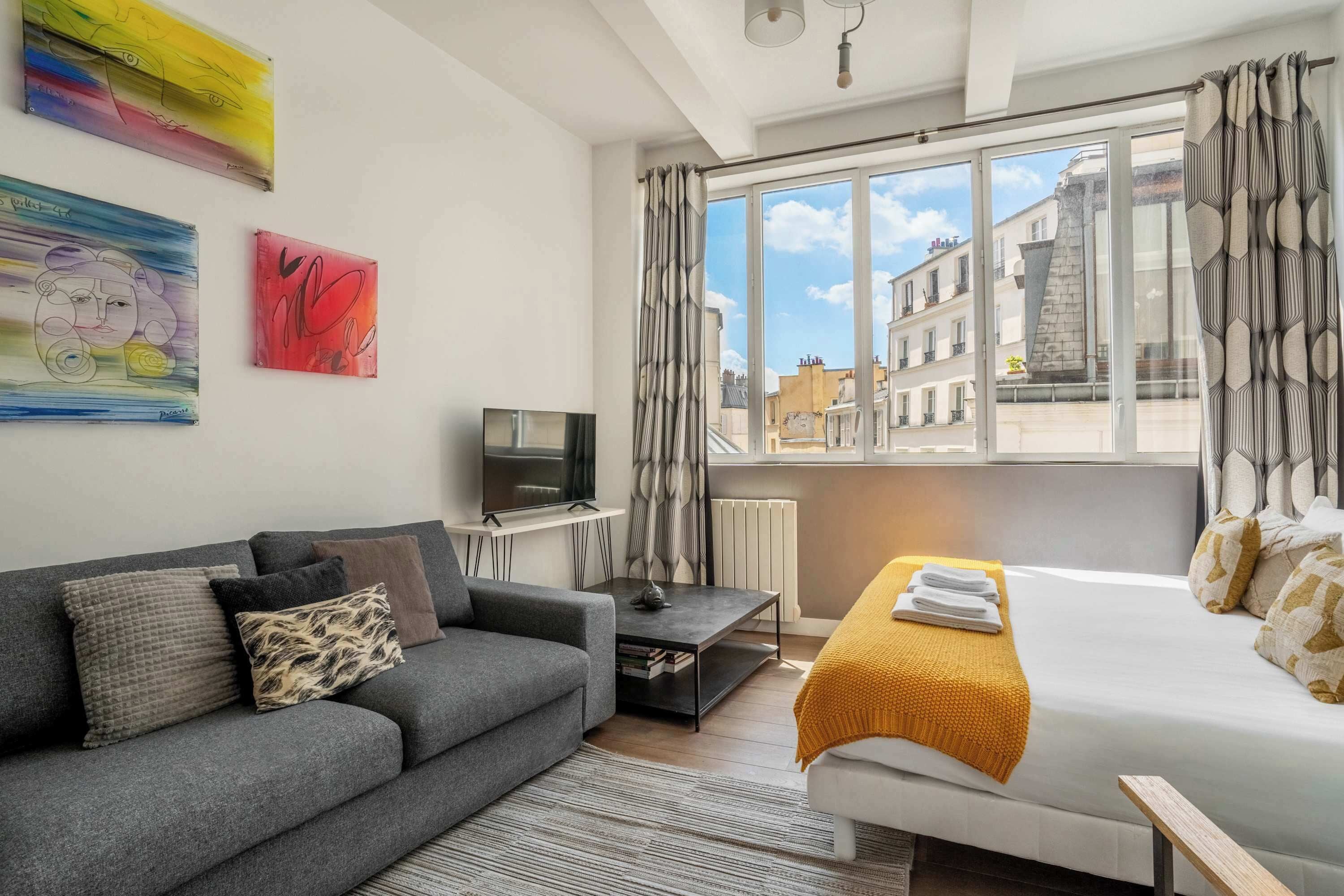 A modern hotel room with a sofa, a bed, a TV, and artwork on the wall.