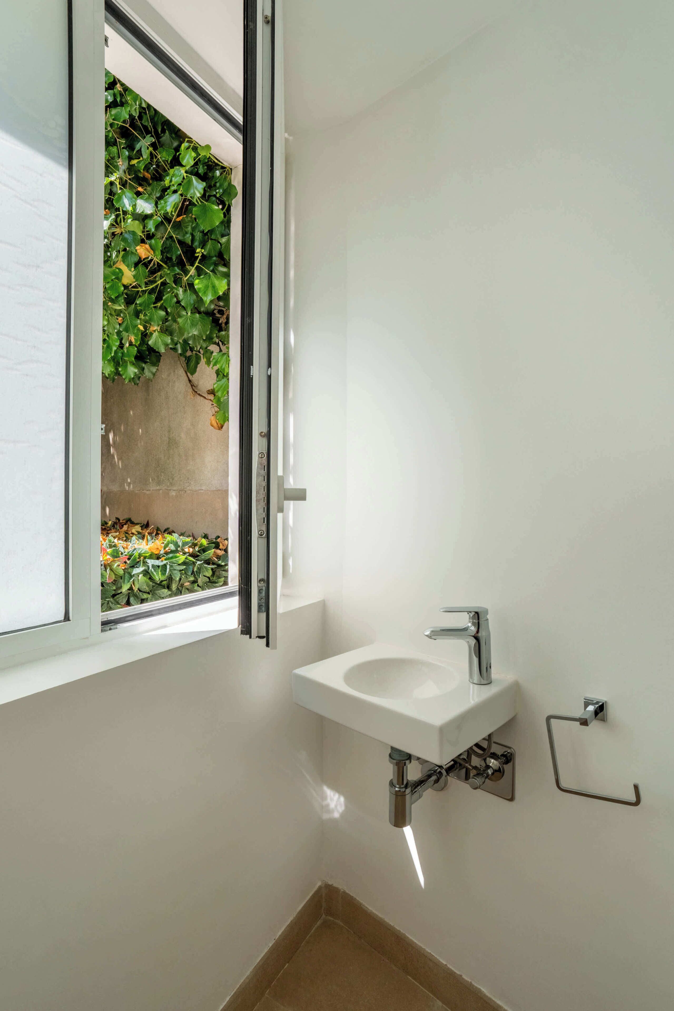 A bathroom with a white sink, a window with a view of greenery, and a towel rack.