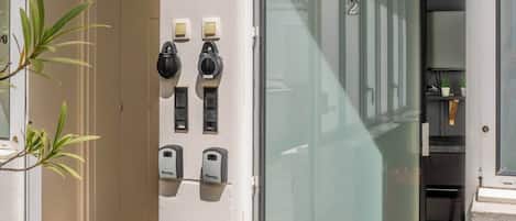 L’entrée d’un hôtel, avec une porte en verre, un système d’accès à code et une petite plante d’intérieur.