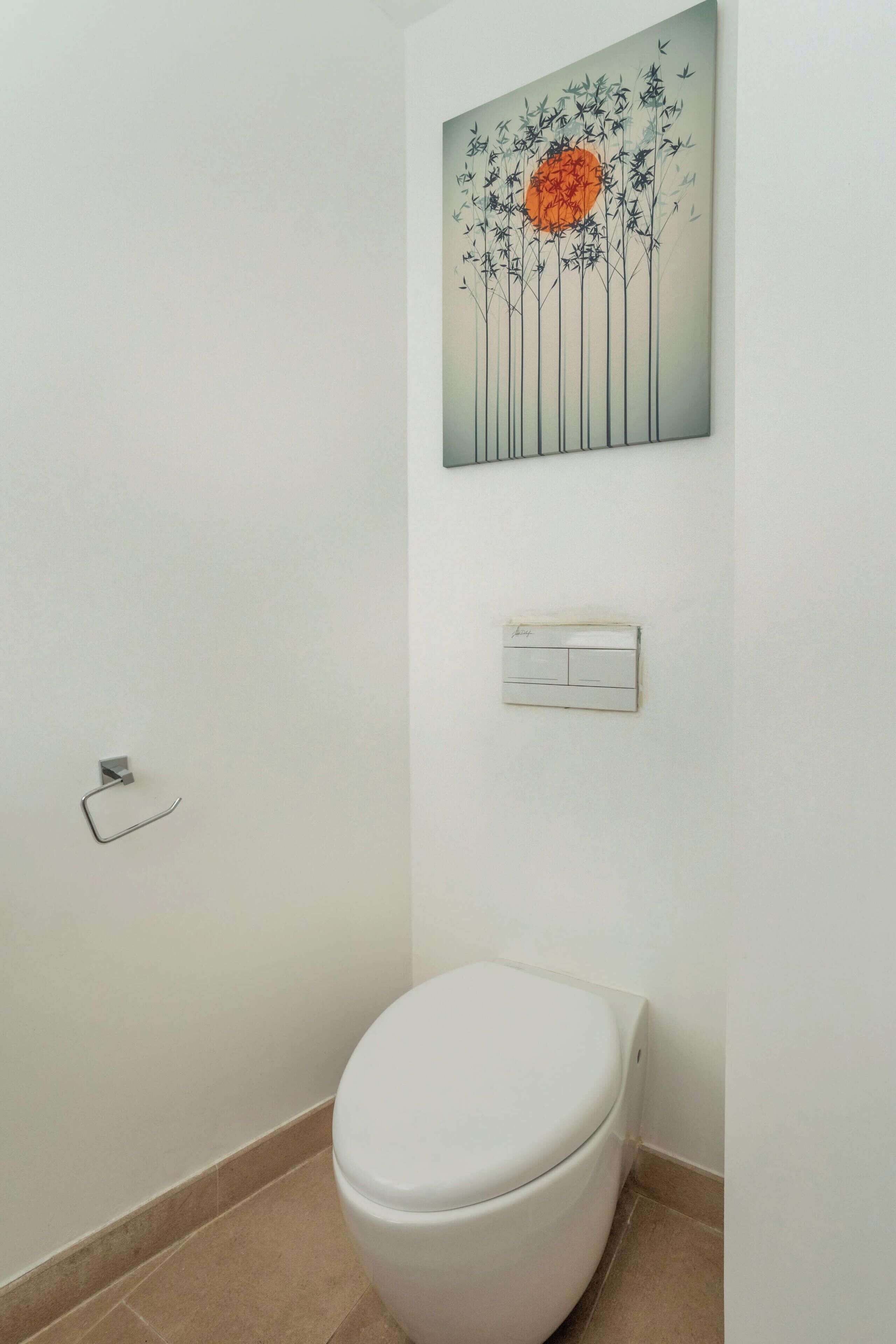 A bathroom with a toilet, a wall-mounted light switch, and a framed artwork above the toilet.