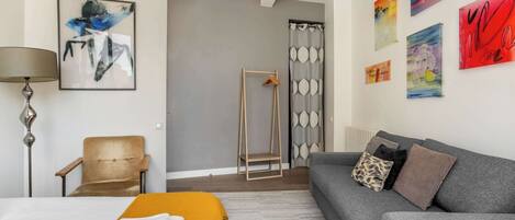 A modern hotel room with a bed, a sofa, a chair, a standing shower, and artwork on the walls.