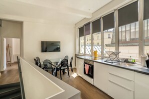 Een moderne keuken met een eethoek, grote ramen en een aan de muur bevestigde televisie.