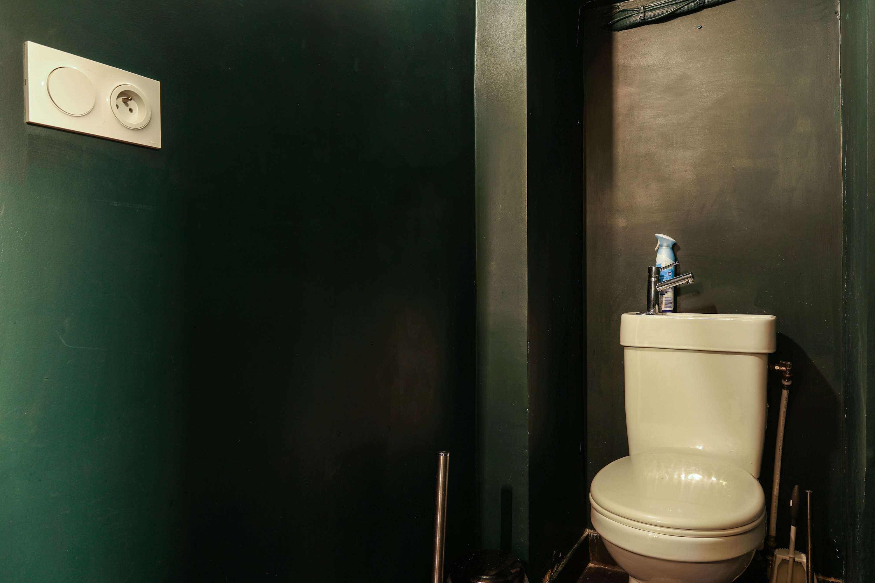 Een toilet met een bidetfunctie, een bedieningsknop aan de muur en een zichtbare leiding.