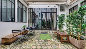A courtyard with stone flooring, a wooden bench, a table with chairs, and potted plants. - Stylish and sunny 7BD with garden for 17 guests! (Paris)