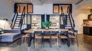 A modern dining area with a wooden table and chairs, a sofa, and a staircase leading to an upper level. - Stylish and sunny 7BD with garden for 17 guests! (Paris)