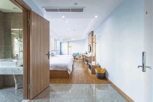 Quarto de hotel com banheiro, cama, escrivaninha e armário.