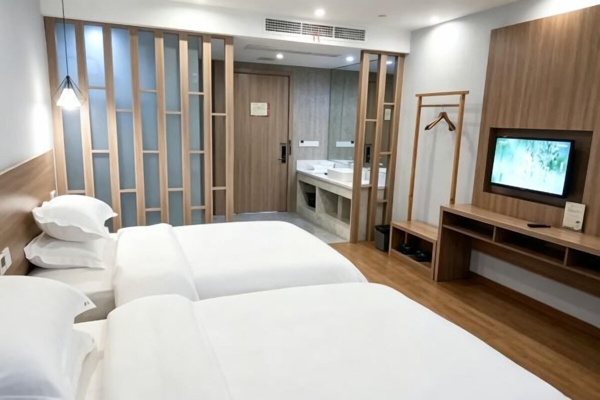 Ein Hotelzimmer mit zwei Betten, einem Fernseher, einem Holzschrank und einem Badezimmer mit Waschbecken und Spiegel.